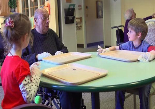 کودکان مقطع پیش‌دبستانی پشت یک میز با سالمندان درس می‌خوانند + تصاویر